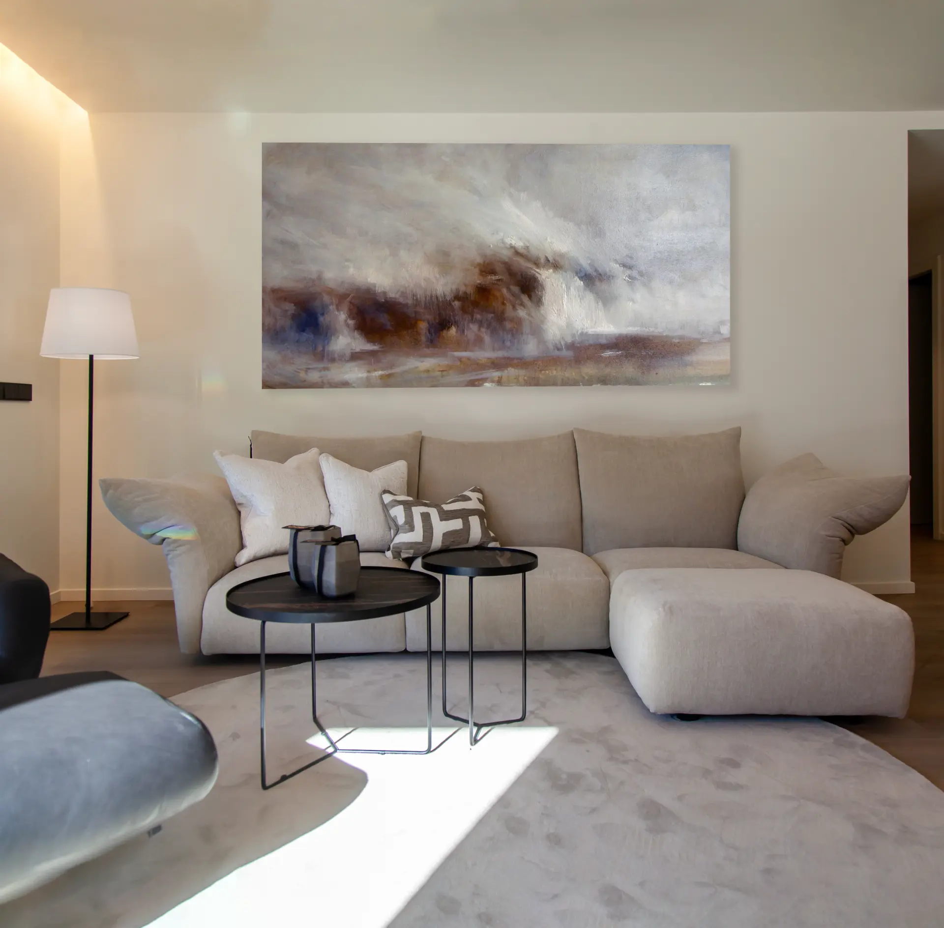 Sala d'estar amb sofà cru i taules de centre negres sota una gran obra abstracta