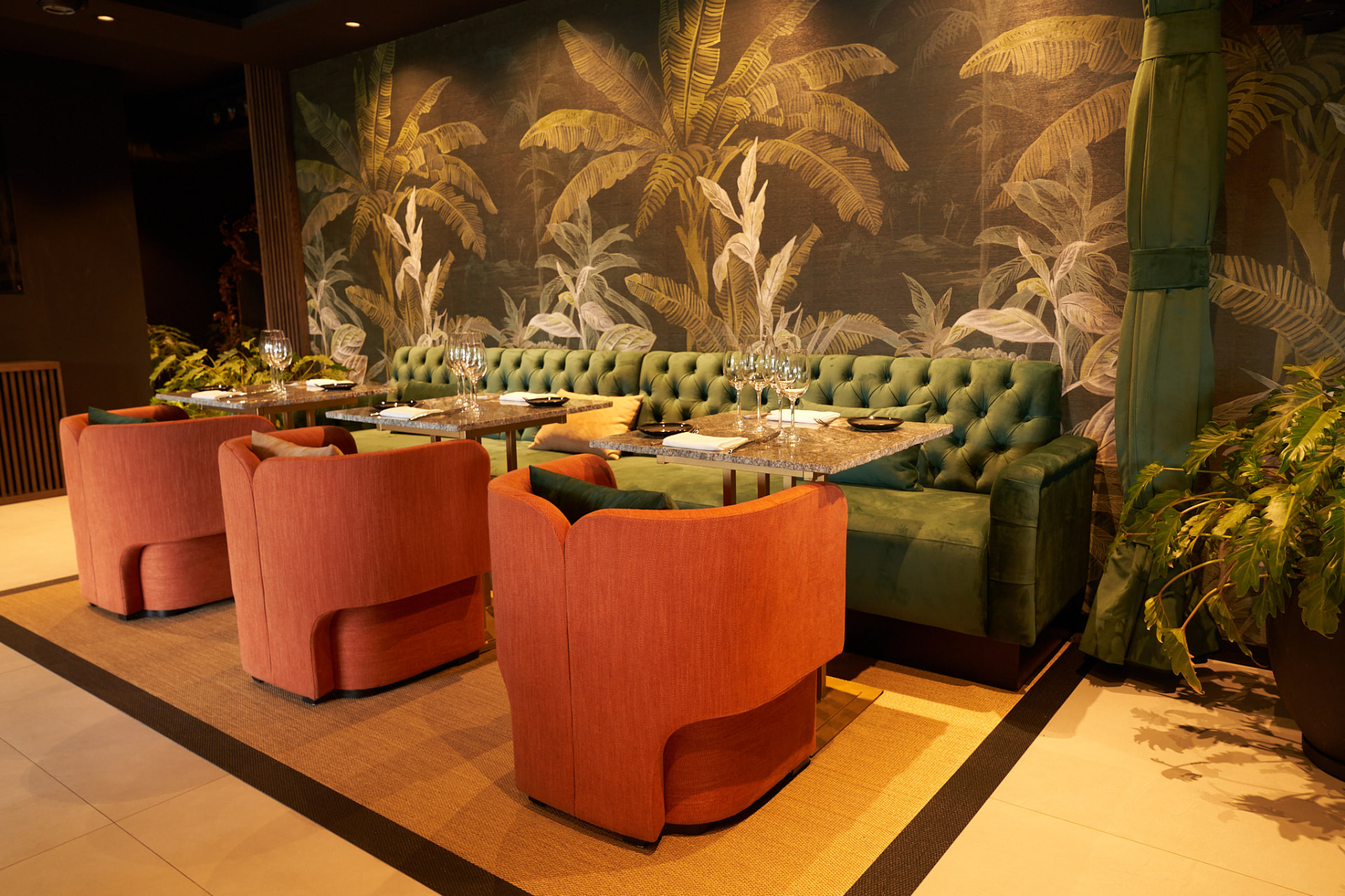 Sala del restaurant amb banquetes de vellut verd, mural botànic i butaques terracota